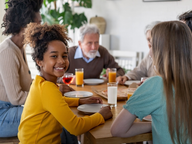 家族と一緒に食卓を囲み、カメラに向かって微笑む少女。